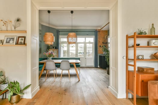 Stylish dining room featuring wooden floors, hanging light fixtures, a dining table, and greenery, creating a cozy yet modern atmosphere.