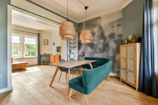 A stylish living room featuring a wooden table, teal chairs, and unique lighting. Fresh flowers add a touch of nature to the contemporary space.