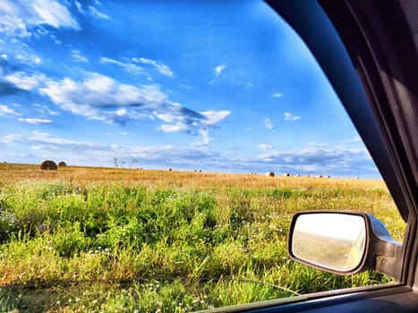 A vast open countryside features golden fields and scattered hay bales under a bright blue sky with fluffy clouds.