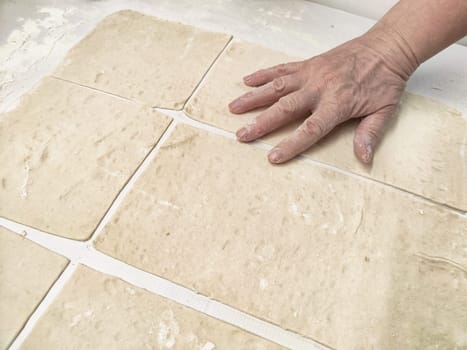 A hand presses down on freshly rolled dough, dividing it into even rectangular pieces on a clean work surface in a bright kitchen.