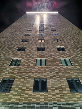 A towering structure stands illuminated during the night, surrounded by a clear sky, showcasing its architectural design from a low perspective.