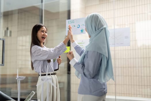 Smiling in excitement, two women celebrate their collaborative efforts in driving ESG initiatives during a productive work session.