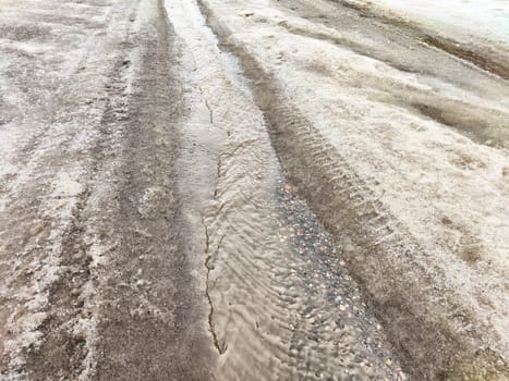 Water fills the tire tracks on a rural dirt road after heavy rainfall, creating muddy conditions and uneven surfaces.