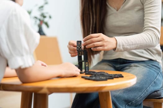 In a family setting, a mother guides her daughter in stacking dominoes, creating a structure while having fun and fostering creative thinking.