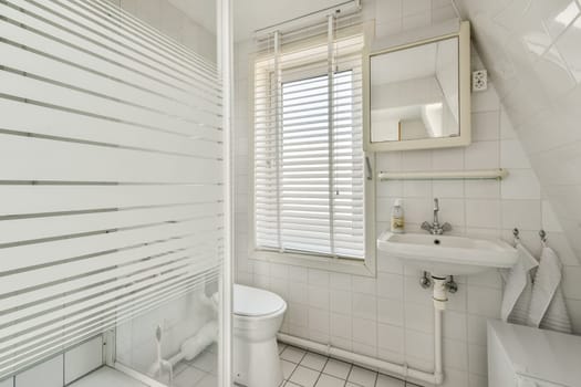 A sleek and modern minimalist bathroom featuring white tiled walls, a contemporary sink, and a stylish shower with frosted glass. Natural light pours in from a window.