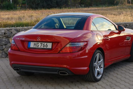 Gaziveren Cyprus -16.04.2025 A striking red sports car elegantly parked near a weathered stone wall, surrounded by golden fields under a serene evening sky radiating warmth and possibilities.
