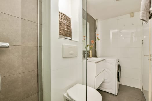 A stylish modern bathroom featuring a glass shower, toilet, washing machine, and elegant floral arrangements that enhance the decor.