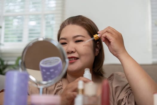 A woman is focused on applying a skin serum, showcasing her commitment to skincare while highlighting the joy of her beauty routine with numerous products displayed around her.
