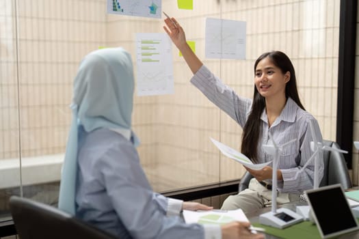 Leveraging visual aids, one woman passionately presents her ideas about sustainability initiatives, engaging her colleague in a dynamic discussion about implementation and impact.