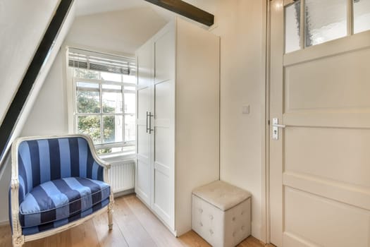 Bright and inviting room featuring a blue striped chair, a stylish cabinet, and natural light streaming through the windows, creating a warm ambiance.