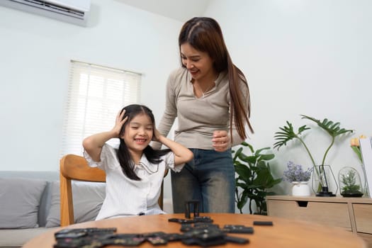 The mother and daughter share laughter and joy while playing with dominos, emphasizing the importance of family interactions in personal growth and creativity.