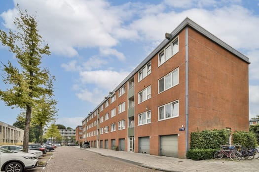 A contemporary brick residential building surrounded by trees and a paved street, showcasing urban living dynamics in a scenic neighborhood.
