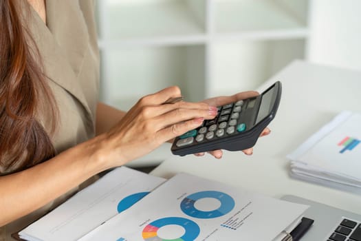 A focused woman uses a calculator while reviewing financial documents, demonstrating diligence in budget management and financial planning.