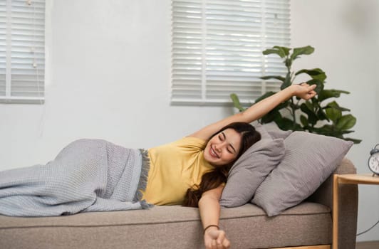 A young woman stretches her arms with a bright smile, enjoying the morning sun in her living room. This moment captures the happiness of starting the day with positivity.
