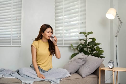 In a serene setting, a young woman sits comfortably, sipping water and starting her day with a focus on hydration and health.