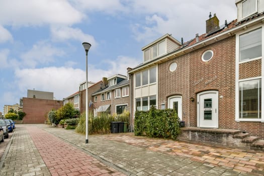 A picturesque urban street featuring brick houses, well-kept gardens, and cobblestone pathways. Bright skies enhance the serene atmosphere, inviting leisurely strolls.