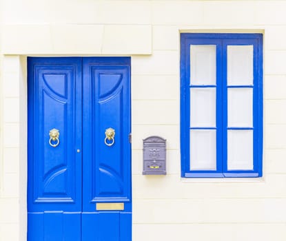 White brick wall with a blue window, door and a grey metal mail box.