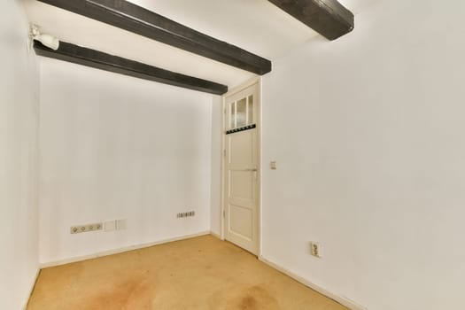 A minimalistic interior room featuring white walls, wooden beams, and a simple door, offering a clean and spacious atmosphere.