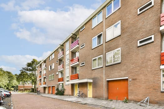 A contemporary red brick apartment complex featuring large windows and a vibrant facade. Surrounded by greenery, it embodies modern urban living.