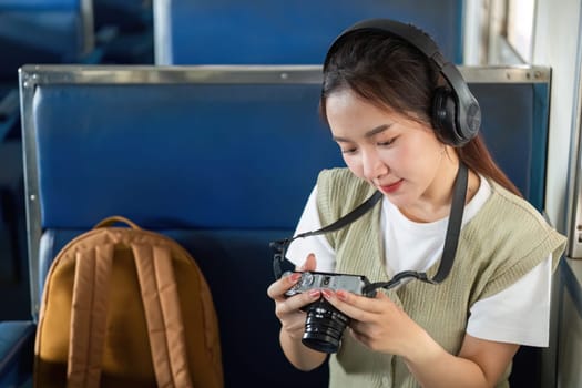 A young woman sits comfortably in a train, focused on her camera as she reviews photos, embodying the essence of a passionate photographer during her travels.