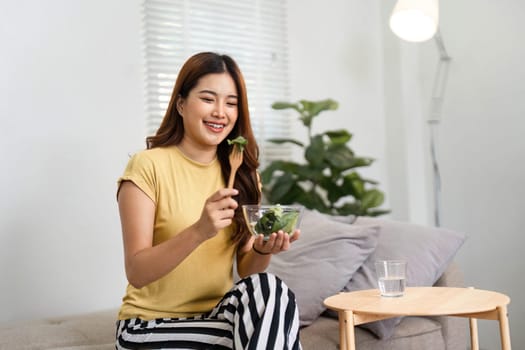 Bright and joyful, a woman is ready to dig into her fresh salad at home, reflecting a commitment to well-being during her morning routine.