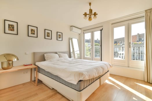 A bright and modern bedroom featuring a comfortable bed, wooden flooring, and large windows that invite sunlight, creating a serene atmosphere.