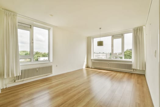 Spacious, airy interior featuring large windows that flood the room with natural light. The minimalist design emphasizes open space and warm wooden flooring.