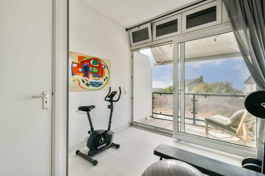 A contemporary interior featuring a stationary bike and colorful artwork, along with large windows that invite natural light and showcase outdoor views.