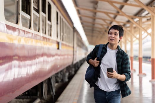 Eager to embark on his adventure, a young traveler rushes towards the train platform while checking his phone for updates.