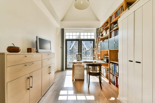 A bright and spacious study room featuring a stylish desk, shelves filled with books, and natural light streaming through a large window.