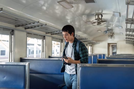 In the calm atmosphere of a train, a young traveler walks through the aisles, using his phone as a guide for his journey.