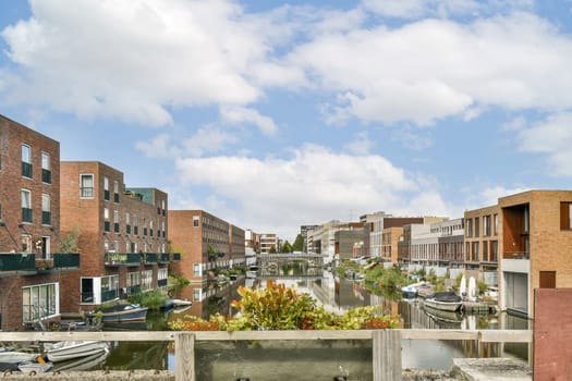 A picturesque view of a tranquil waterfront lined with modern residential buildings, lush greenery, and colorful reflections on the water under a cloudy sky.