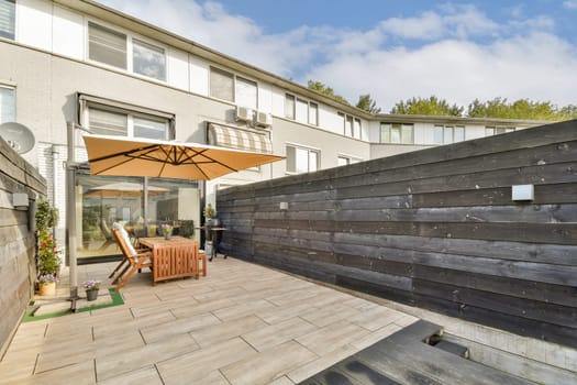 A stylish outdoor patio featuring wooden furniture, an umbrella for shade, and landscaped greenery. Ideal for relaxation and entertaining guests in a modern setting.