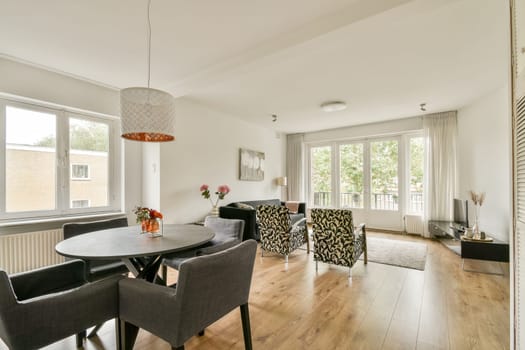 A bright and airy living room featuring contemporary furniture, large windows allowing natural light, and a stylish dining area combined with soft decor elements.