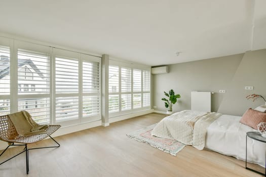 A stylish, modern bedroom featuring a soothing color palette, minimal furniture, and ample natural light from large windows adorned with blinds.