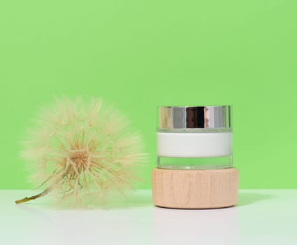 Glass jar with cream and dandelion on a green background, skin care cosmetics