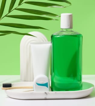 Refreshing mouthwash in a transparent plastic bottle and dental floss, white tube on a green background