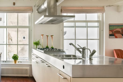 A sleek and contemporary kitchen featuring a metallic island, stylish decor, and ample natural light streaming through large windows.