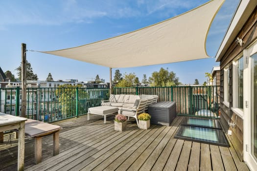 A stylish rooftop patio features comfortable seating, planters, and a protective shade sail, offering a relaxing outdoor space with a view.