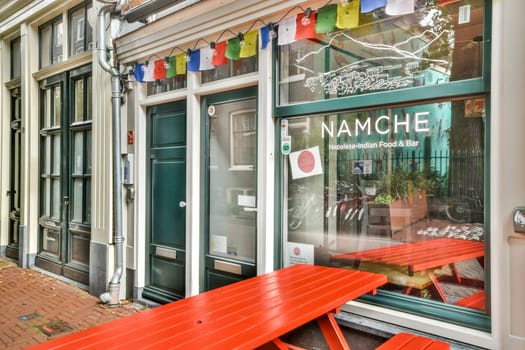 An inviting restaurant exterior featuring vibrant red tables, colorful prayer flags, and a welcoming window display. Perfect for enjoying food and drinks outside.