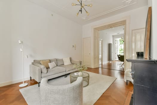 A contemporary living room featuring a stylish grey sofa, elegant decor, and natural light streaming through spacious entries. The design emphasizes comfort and minimalism.