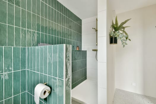 Stylish bathroom featuring a green tiled shower area with contemporary fixtures and minimalistic decor. A touch of nature is introduced with a potted plant.