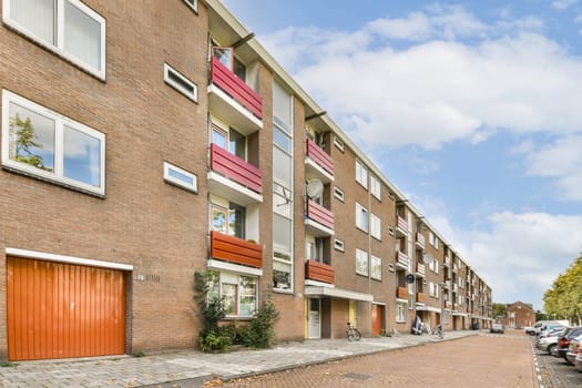 A modern residential building featuring brick architecture and vibrant balcony designs, located on a peaceful street lined with trees and parked bicycles.