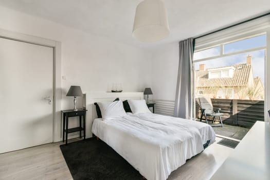 A stylish minimalist bedroom featuring a double bed, nightstand, and large windows allowing plenty of natural light. Simple decor enhances the serene atmosphere.