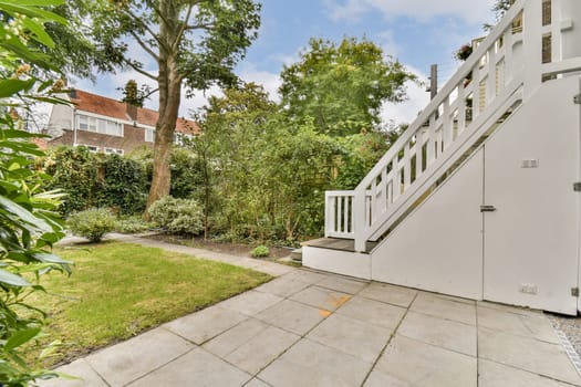 A peaceful garden scene featuring a stone pathway leading to a staircase, surrounded by lush greenery and trees under a blue sky.