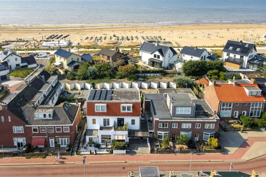Aerial view showcasing coastal houses lined along a sandy beach, with umbrellas and sunbathers in the distance. Emphasis on architecture and natural beauty.
