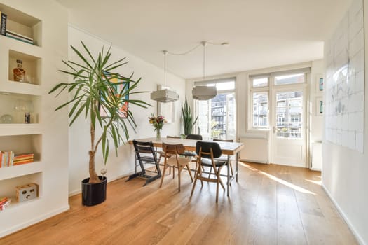 Bright and airy modern dining area featuring a large window, wooden flooring, and stylish furniture surrounded by greenery, creating a welcoming atmosphere.