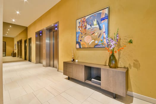 A spacious hotel lobby featuring an elegant wooden console, abstract artwork, and a colorful floral arrangement. The ambient lighting enhances the inviting atmosphere.
