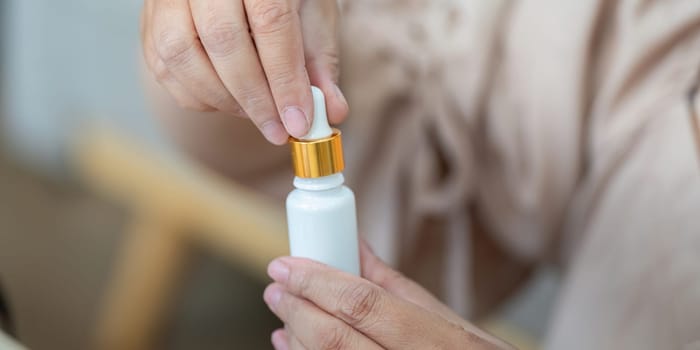 Focusing on precision, a woman unscrews the cap of a skincare dropper bottle, ready to enhance her beauty routine.