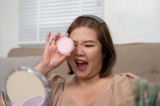A woman playfully holds a beauty sponge, excited about her makeup application and enjoying her beauty routine.